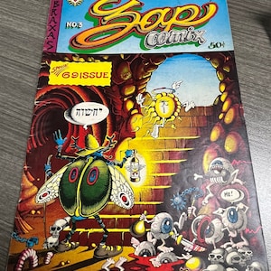 May include: A comic book cover with a green and blue beetle character holding a lantern. The cover is titled "Zap Comix" and features a psychedelic design with a sun-like figure and a cave entrance. The text "Special! 69 Issue" is visible in a red box.