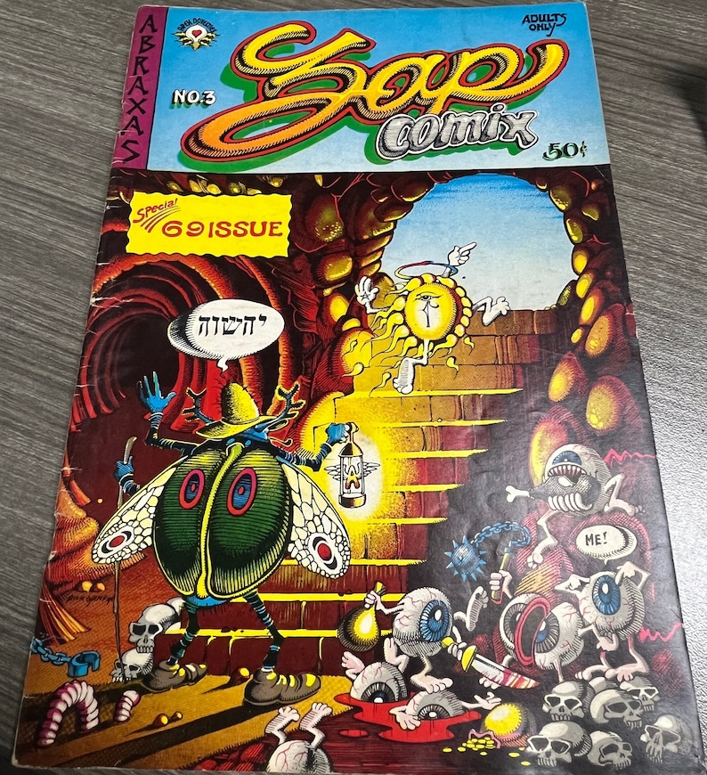 May include: A comic book cover with a green and blue beetle character holding a lantern. The cover is titled "Zap Comix" and features a psychedelic design with a sun-like figure and a cave entrance. The text "Special! 69 Issue" is visible in a red box.