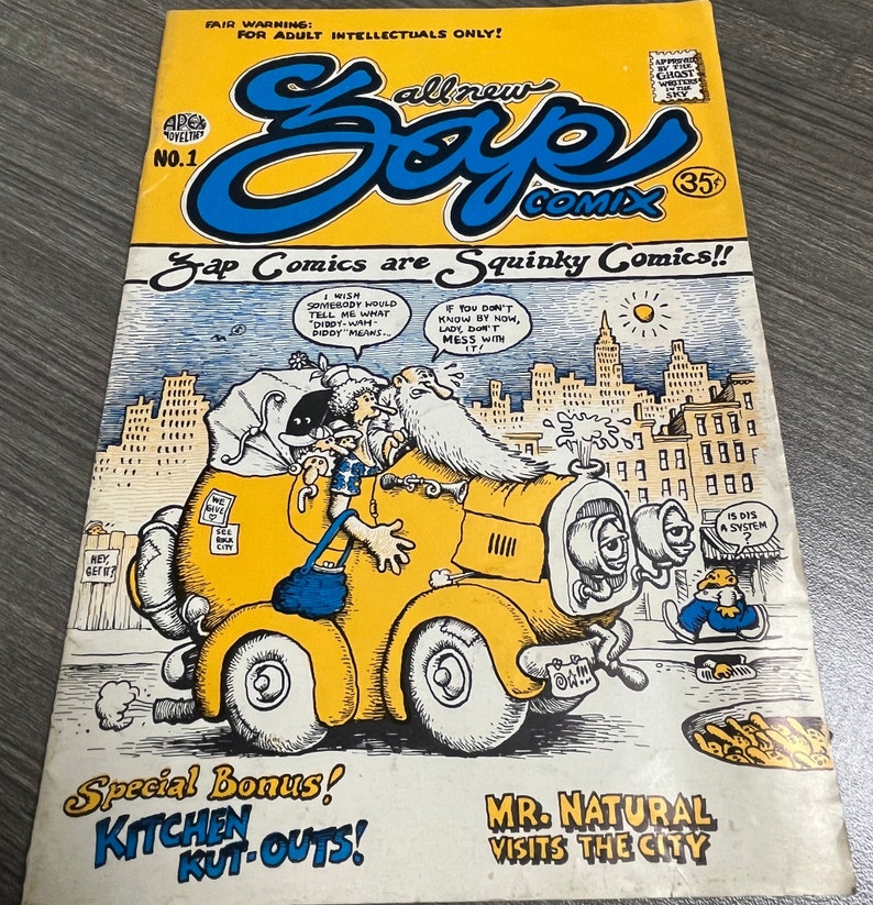 May include: A comic book cover with a yellow car and a man with a long white beard. The cover is titled "Zap Comics are Squinky Comics!" and features the text "All New Zap Comics" and "Special Bonus! Kitchen Kut-Outs!" The cover also features the text "Mr. Natural Visits the City".