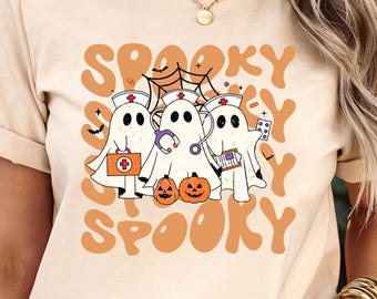 May include: Beige t-shirt with a Halloween design. The graphic shows three ghost characters dressed as nurses, holding medical supplies, and the word "Spooky" in orange bubble letters. Two small pumpkins are also included.