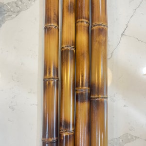 May include: Four natural bamboo poles with a light brown color and dark brown stripes. The poles are arranged vertically and are in focus.