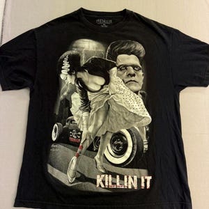 May include: Black t-shirt with a graphic of Frankenstein and his bride, and the text "KILLIN IT". The design includes a vintage car and lightning effects, creating a classic horror movie theme. The t-shirt has a crew neck.