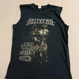 May include: A black sleeveless t-shirt featuring a graphic print of a statue and the text HELLYEAH at the top. Below the statue, the text reads I'VE BEEN DAMAGED LEFT IN RUIN in a distressed font. The shirt has raw, cut-off armholes and a crew neckline.