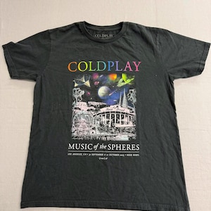 May include: Black t-shirt featuring the band Coldplay. The shirt has the band's name in colorful letters above a graphic of a concert scene with a Ferris wheel and the text "MUSIC of the SPHERES". The shirt also has the text "LOS ANGELES, CA • 30 SEPTEMBER • 6 OCTOBER 2023 • ROSE BOWL".
