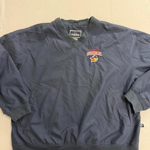 Puede incluir: Chaqueta cortavientos azul marino con cuello en V y un pequeño bolsillo. La chaqueta cortavientos tiene dobladillo y puños acanalados. El texto "Holloway" está en el cuello. El texto "Mound Hens" y un logotipo están en el pecho izquierdo.