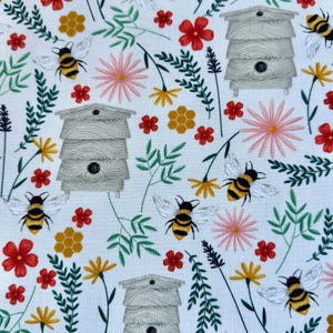 May include: A white fabric with a repeating pattern of bees, flowers, and beehives. The bees are yellow and black, the flowers are red, pink, and yellow, and the beehives are gray.