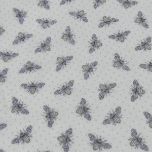 May include: Close-up of a white fabric with a repeating pattern of bees and small gray dots. The bees are detailed with gray and purple wings, and the overall design has a vintage or cottagecore aesthetic.