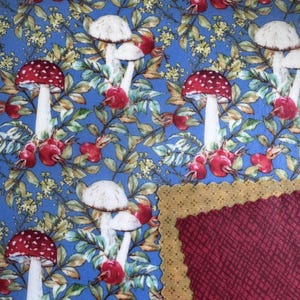 May include: A fabric swatch featuring a blue background with a repeating pattern of red-capped mushrooms, red berries, and green leaves. A section of burgundy fabric with a textured pattern and a gold-edged border is visible.