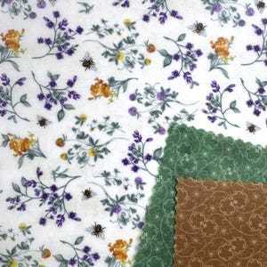 May include: A white fabric with a floral pattern featuring purple, yellow, and orange flowers, green leaves, and bees. Two pieces of fabric with scalloped edges are in the lower right corner, one green and one brown with a floral design.