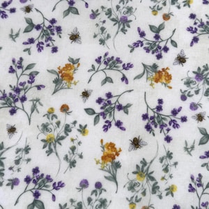 May include: White fabric with a repeating pattern of purple and yellow wildflowers, green leaves, and small bees. The floral design is scattered across the fabric, creating a natural and whimsical aesthetic. The bees add a touch of detail.
