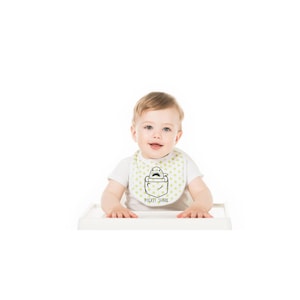 May include: A baby wearing a white bib with green polka dots and a black and white illustration of a shark in a pocket. The bib has the text "Pocket Shark" printed on it.