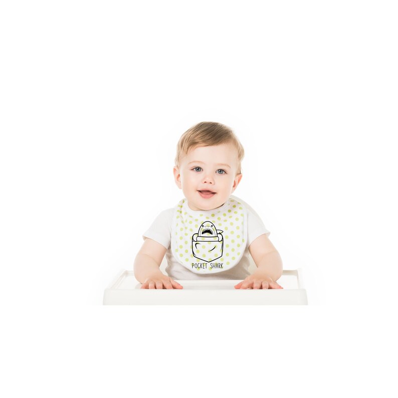 May include: A baby wearing a white bib with green polka dots and a black and white illustration of a shark in a pocket. The bib has the text "Pocket Shark" printed on it.