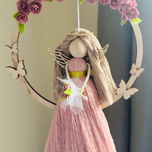 May include: A pink yarn angel doll with a wooden head and wings, hanging from a wooden hoop decorated with pink felt flowers.