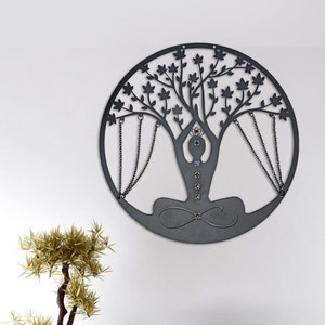 May include: A black metal tree of life wall decor with a yoga figure in the center. The tree has branches with leaves and chains hanging from them. The yoga figure has seven colorful gemstones on its body.