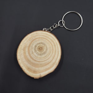 May include: A wooden keychain with a round, light brown wood disc with concentric rings. The disc is attached to a silver metal key ring.