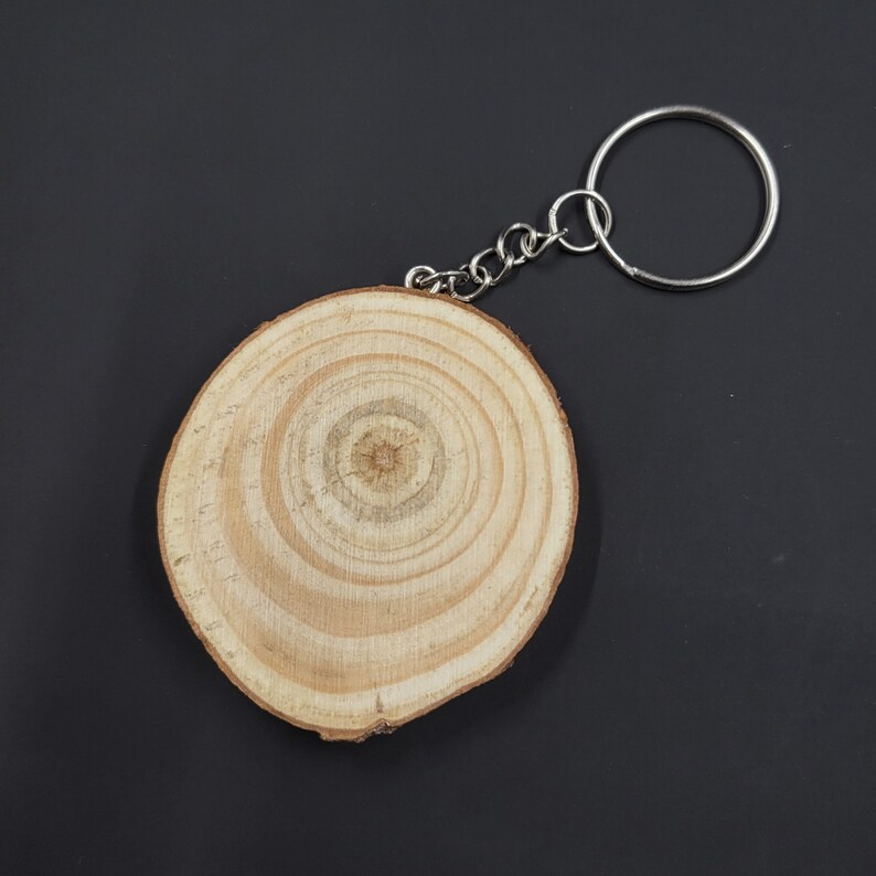 May include: A wooden keychain with a round, light brown wood disc with concentric rings. The disc is attached to a silver metal key ring.
