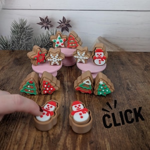 May include: A selection of Christmas-themed gingerbread-style ornaments. The ornaments feature stars, Christmas trees, and snowmen, decorated with red, white, and green icing. The word "CLICK" is visible in the image.