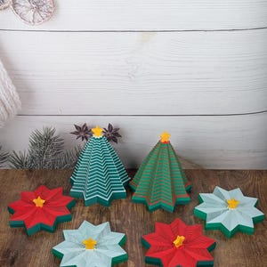 Könnte beinhalten: Eine Sammlung von Weihnachtsdekorationen, darunter zwei grün-weiß gestreifte Weihnachtsbäume mit gelben Sternen und mehrere rot- und hellblaue sternförmige Untersetzer mit gelben Sternen in der Mitte. Die Dekorationen befinden sich auf einer Holzoberfläche.