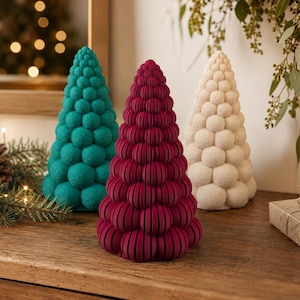 May include: Three conical decorative trees in teal, deep magenta, and cream. Each tree features a textured surface composed of stacked, rounded, spherical segments arranged in a vertical, tapering pattern from a wide base to a pointed top.