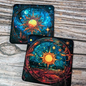 Pode incluir: Dois  copos de apoio quadrados com um design celestial. Os copos de apoio apresentam um design circular com um sol no centro, rodeado de estrelas e planetas. O copo de apoio superior tem um fundo azul com um sol dourado, enquanto o copo de apoio inferior tem um fundo azul escuro com um sol amarelo.