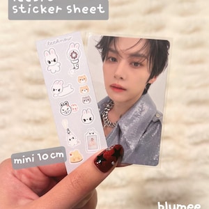 May include: A 10 cm sticker sheet labeled leebit sticker sheet featuring various white rabbit illustrations, a light stick, and small animal faces, alongside a rectangular photo card of a person with dark hair wearing a silver jacket.
