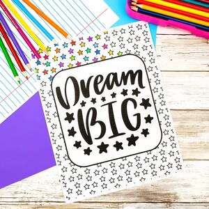 K&ouml;nnte beinhalten: Eine wei&szlig;e Malvorlage mit dem schwarzen Text Dream BIG, umgeben von einem Rand aus kleinen Sternen. Die Seite liegt neben einem Set bunter Stifte und einem violetten Blatt Papier, mit einem Stifteetui, das weitere farbige Stifte enth&auml;lt.