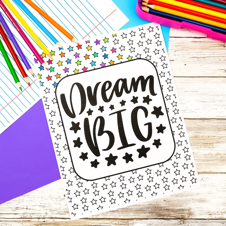 K&ouml;nnte beinhalten: Eine wei&szlig;e Malvorlage mit dem schwarzen Text Dream BIG, umgeben von einem Rand aus kleinen Sternen. Die Seite liegt neben einem Set bunter Stifte und einem violetten Blatt Papier, mit einem Stifteetui, das weitere farbige Stifte enth&auml;lt.