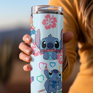 May include: A blue and white stainless steel tumbler with a design featuring Stitch from Lilo & Stitch. The design includes Stitch with hearts, flowers, and crayons.