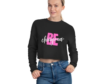 May include: A black cropped sweatshirt with long sleeves featuring the text "BE chingona" in pink lettering with a small heart symbol.