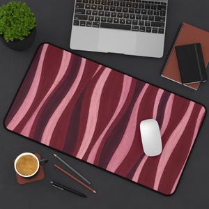May include: A rectangular desk mat featuring a repeating pattern of vertical, wavy stripes in shades of deep burgundy, dark plum, and soft light pink. The mat has rounded corners and a black border, providing a smooth surface for computer peripherals.