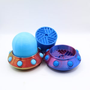 May include: Three 3D printed UFO-shaped objects. One is blue with a light blue dome, one is red with a light blue dome, and one is purple with a light blue dome.