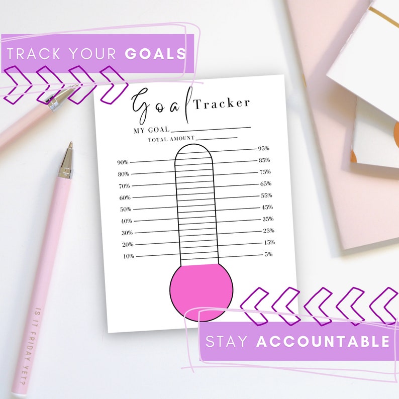 The pink Goal Thermometer is shown on a white desk noting that you can track your goals and stay accountable with pink pens and notebooks surrounding.
