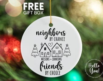 May include: White ceramic Christmas ornament with black text and illustrations. The ornament reads "neighbors by chance, friends by choice" with house and tree graphics. Includes the names "Wilsons + Johnsons". A gold string is attached.
