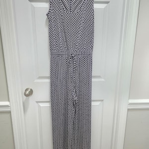 Peut inclure: Une combinaison sans manches avec un motif en losanges bleu marine foncé et blanc. Le vêtement présente une encolure en V, une taille resserrée par un cordon de serrage et un pantalon long à jambes droites. Le tissu arbore un imprimé géométrique.
