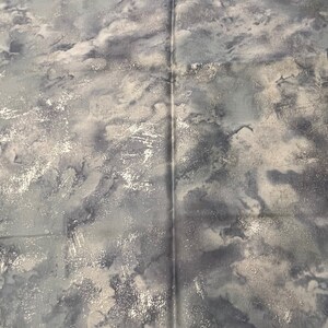 May include: A close-up of a gray and white fabric with a marbled pattern. The fabric has a subtle shimmer and a textured surface.