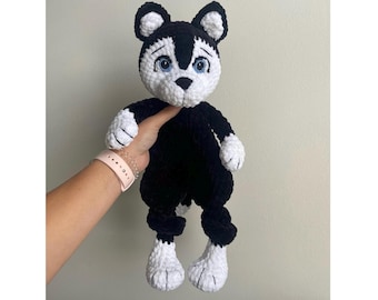 May include: A black and white crocheted stuffed animal with a long tail and big eyes. The animal is wearing a black and white outfit.