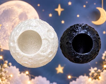 Puede incluir: Dos recipientes esféricos con forma de luna, uno con acabado blanco brillante y otro con acabado negro mate. Ambos artículos presentan una superficie texturizada con detalles realistas de cráteres y una gran abertura circular en el frente.