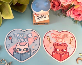 May include: Two heart-shaped stickers with a cat and a dog reading books. The cat sticker is blue and says "Pass the Yaoi" and the dog sticker is pink and says "Pass the Yuri".