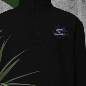 以下が含まれることがあります： 「Commit to Connection」と刺繍された青いロゴが付いた、黒いジップアップスウェットシャツです。