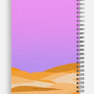 May include: Spiral-bound notebook with a cover featuring a desert landscape design. The top portion of the cover is a gradient of pink and purple, while the bottom has a layered illustration of sand dunes in shades of orange and tan.