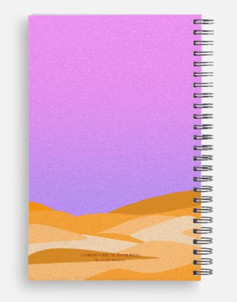 May include: Spiral-bound notebook with a cover featuring a desert landscape design. The top portion of the cover is a gradient of pink and purple, while the bottom has a layered illustration of sand dunes in shades of orange and tan.