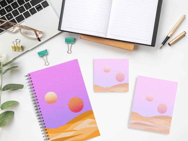 May include: A spiral-bound notebook, sticky notes, and a card featuring a desert landscape with two suns in shades of orange and pink. The notebook and stationery have a purple and orange color scheme. Other office supplies are also visible.
