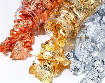 May include: Three glass jars filled with loose gold, silver, and copper leaf flakes. The jars are open and the flakes are spilling out.