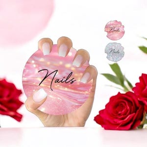 May include: A pink and white ombre nail design with a pink glitter background. The design is on a round sticker with the word "Nails" written in black cursive.