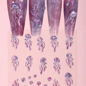 May include: A sheet of iridescent nail art stickers featuring jellyfish, coral, and bubbles. The stickers are on a pink background and have a holographic finish.