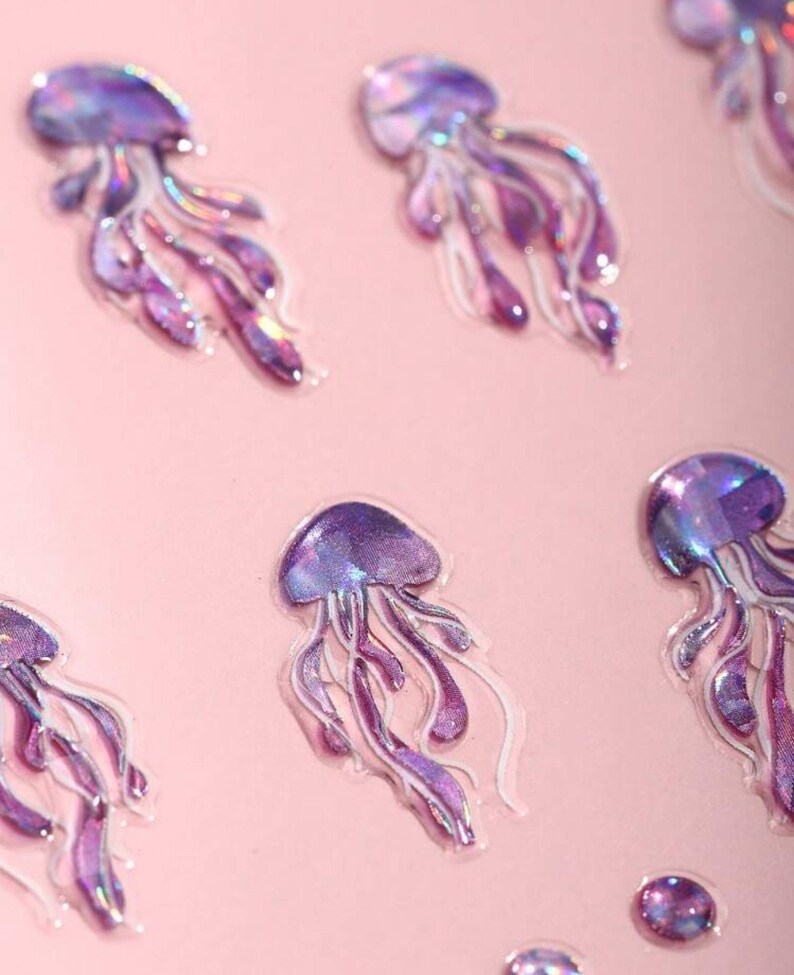 May include: A sheet of iridescent purple and pink holographic jellyfish stickers. The stickers are on a pink background.