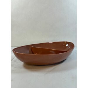 May include: A brown, oval-shaped serving dish with a divider, creating two separate compartments. The dish has a glossy finish and is set against a white background. This versatile dish is suitable for serving snacks or appetizers.