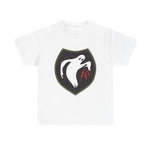 May include: White t-shirt featuring a shield-shaped emblem with a white ghost figure and red lightning bolts. The emblem is outlined in black and green. The shirt is a casual wear item.