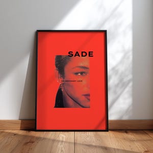 Könnte beinhalten: Ein gerahmtes Poster mit einem Porträt von Sade Adu auf einem leuchtend roten Hintergrund. Das Wort "SADE" ist in fetten, schwarzen Großbuchstaben über dem Bild gedruckt. Der Text "NO ORDINARY LOVE" steht darunter. Der Rahmen ist schwarz.