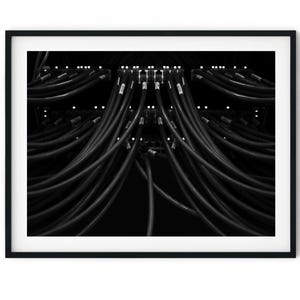 May include: A black and white photograph of a close-up of a network server rack with many black cables plugged in.
